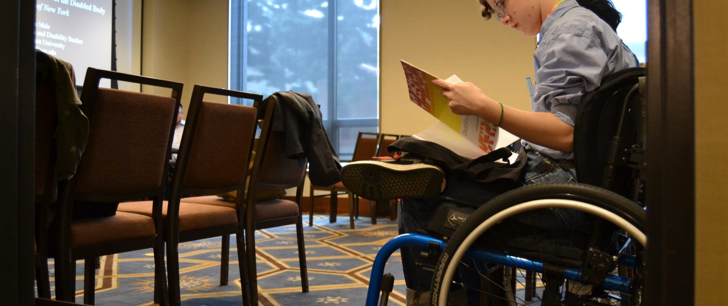 Conference attendee in a wheelchair reading a program booklet.